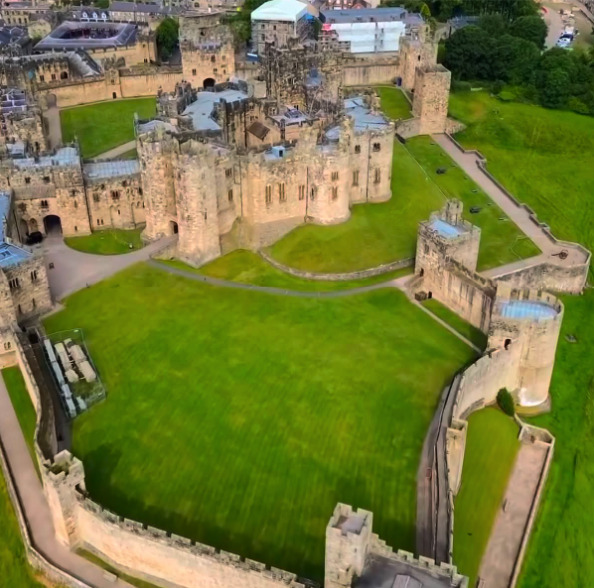 Alnwick Castle and its grounds from above, with the town of Alnwick beyond the walls